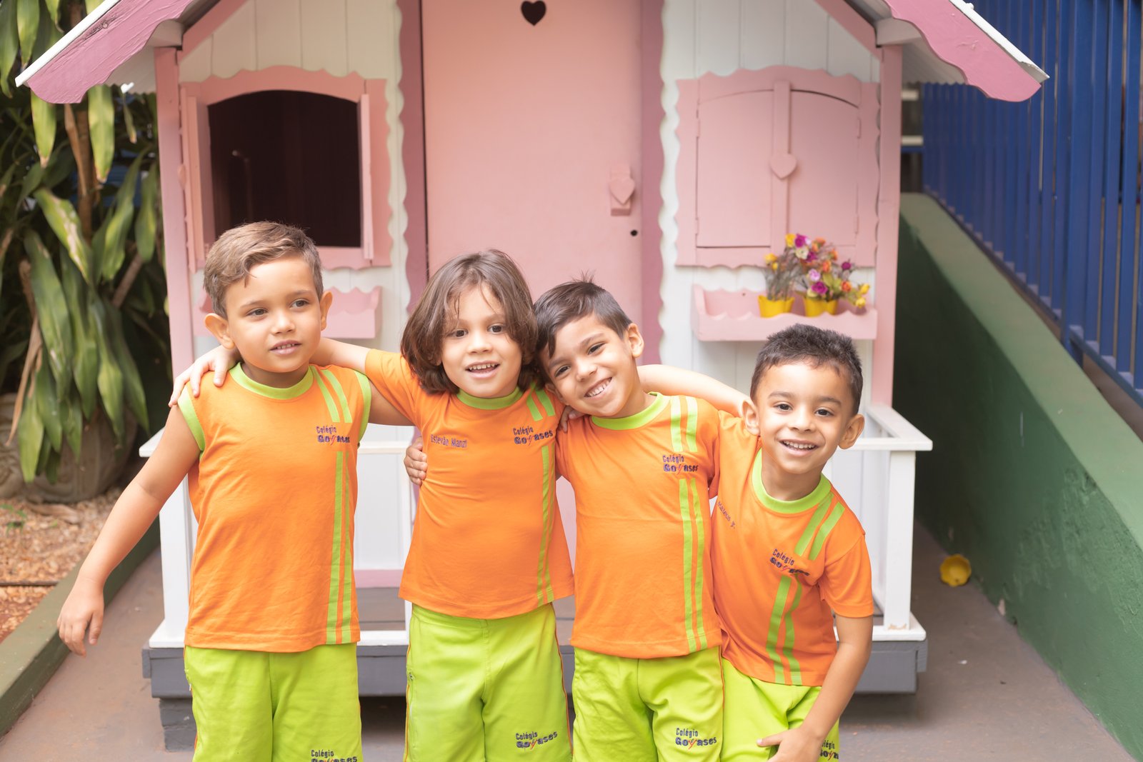 Quatro alunos do Colégio Goyases sorrindo, abraçados, em frente à casinha do playground da Educação Infantil