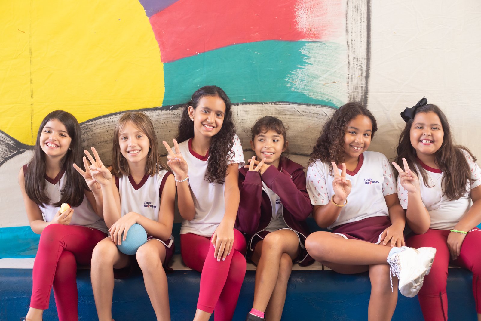 Grupo de alunas dos Anos Finais sorrindo sentadas juntas no pátio