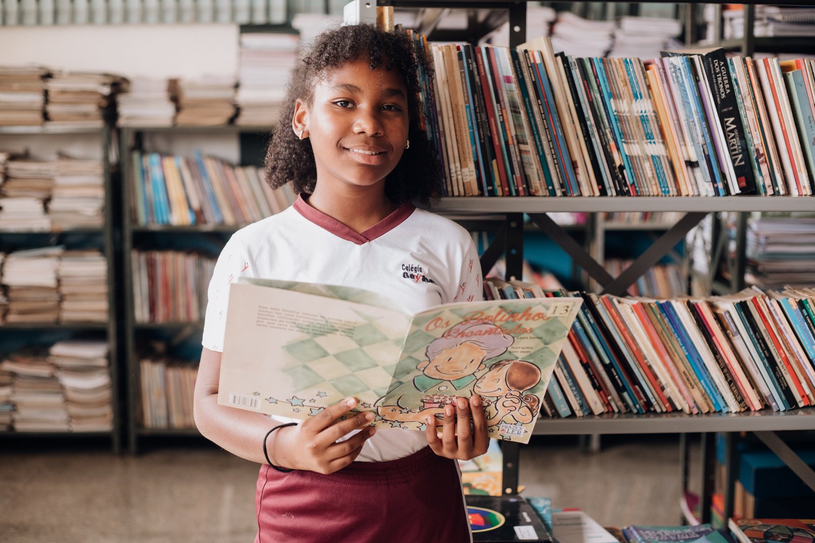 Aluna dos Anos Finais com um livro na biblioteca do colégio